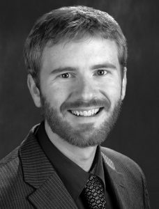Ben-Watters Black and white headshot of a smiling man with a beard wearing a pinstripe suit and a patterned tie.