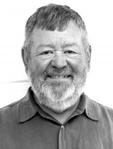 byron Black and white portrait of a smiling elderly man with a beard, wearing a collared shirt and a jacket. he has short, gray hair and a cheerful expression.