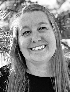 DR-crop Black and white close-up portrait of a smiling woman with long hair, against a blurred natural background.
