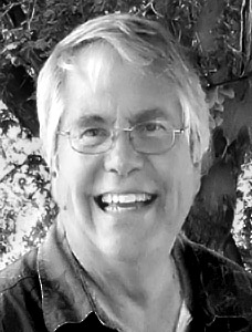 stevef_web-profile A black and white portrait of a smiling elderly man with glasses, featuring short white hair, and wearing a jacket against a leafy background.