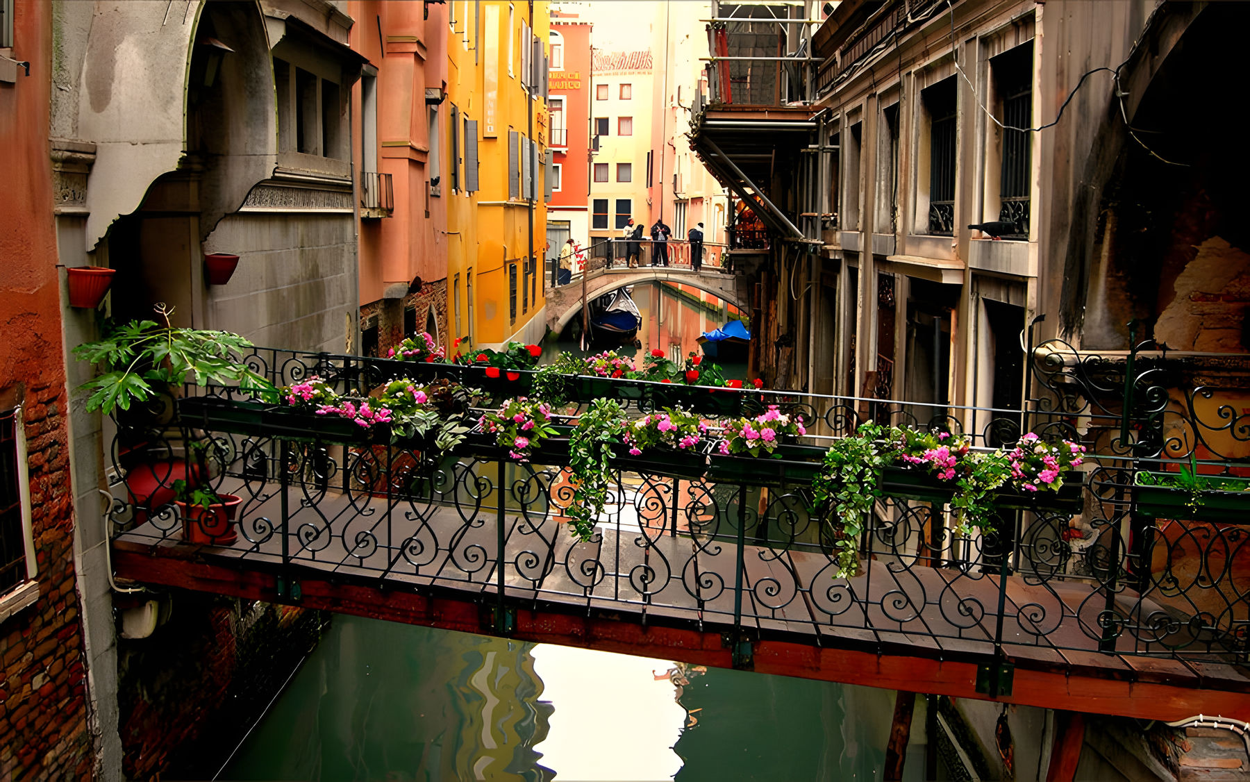 A colorful and quaint venetian canal flanked by vibrant buildings, with a charming wrought-iron bridge adorned with blooming flowers in the foreground.